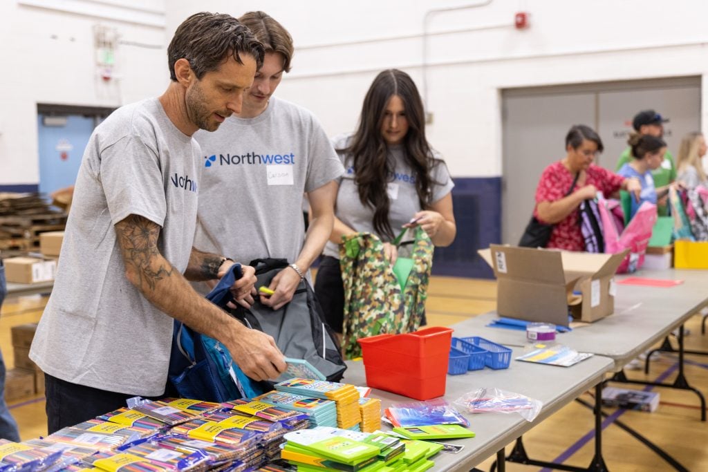 Three NWRA volunteers focused on sorting school supplies on a table.